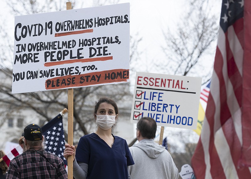 In this April 24, 2020, file photo, a nurse demonstrating in favor of business closures is surrounded by demonstrators against Gov. Tony Evers’ restrictions on daily life due to the coronavirus pandemic at the Capitol in Madison, Wis. Doctors and nurses treating those sick and dying from the coronavirus said politics around social distancing and the lethality of the virus are complicating treatment efforts. story.lead_photo.caption