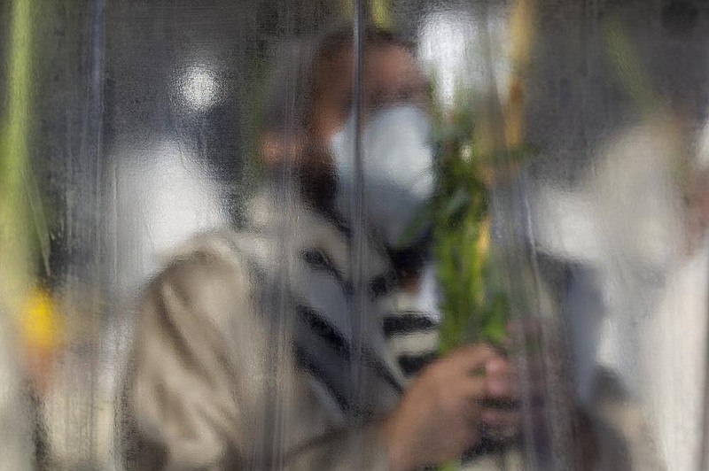 An Ultra-Orthodox Jew prays and holds a branch, one of the four items used as a symbol on the Jewish holiday of Sukkot, on Sunday as he keeps social distancing and separated by plastic partitions during the current nationwide lockdown due to the coronavirus pandemic in the Orthodox Jewish neighborhood of Mea Shearim in Jerusalem
(AP/Ariel Schalit)