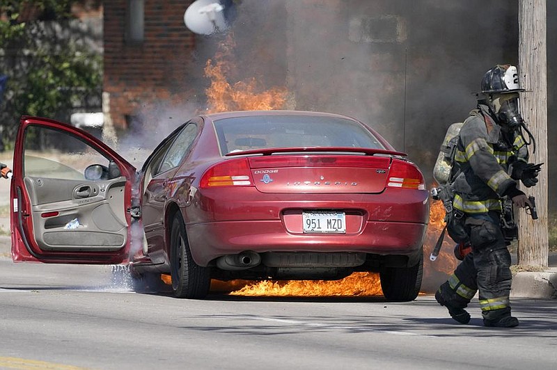 A firefighter removes a weapon from a burning car Tuesday in Wichita, Kan. The driver had alerted firefighters to the weapon so they could safely remove it. (AP/Orlin Wagner) 
