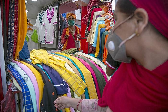 A woman looks at the items on display Tuesday at a clothing store in Kathmandu, Nepal, as a holy man waits for alms at the store’s entrance. (AP/Niranjan Shrestha) 