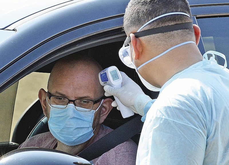 Arizona Army National Guard Pvt. Ronald Aguilar takes the temperature of a man at a drive-thru coronavirus testing site Saturday on the main campus at Arizona Western College in Yuma.
(AP/The Yuma Sun/Randy Hoeft)