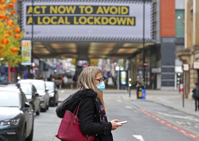 A woman wearing a face mask walks in Manchester, England, Monday, Oct. 19, 2020.