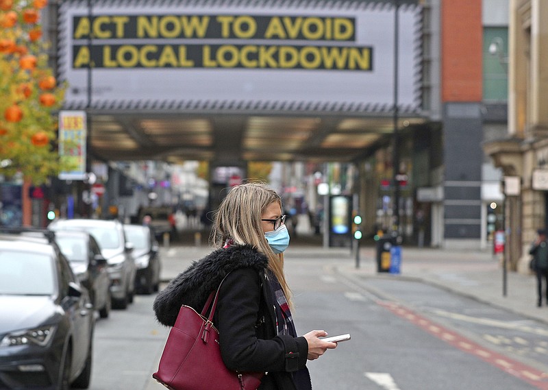 A woman wearing a face mask walks in Manchester, England, Monday, Oct. 19, 2020. Britain’s government says discussions about implementing stricter restrictions in Greater Manchester must be completed Monday because the public health threat caused by rising COVID-19 infections is serious and getting worse.