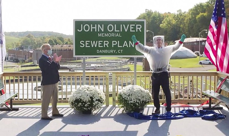 This image taken from video released by HBO shows John Oliver, host of "Last Week Tonight with John Oliver," right, with Mayor Mark Boughton during a dedication ceremony for The John Oliver Memorial Sewer Plant, in Danbury, Conn. Oliver made a secret trip to Connecticut last week to help cut the ribbon on a sign naming a sewage treatment plant in his honor. (HBO via AP)