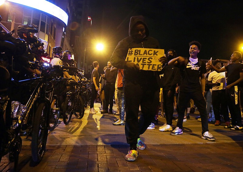 Protesters hold signs and walk past a line of police in downtown Columbus, Ohio, in this Thursday, May 28, 2020, file photo. A federal prosecutor announced Friday, Oct. 23, 2020, that she has charged a Texas man with traveling across state lines to participate in a riot, accusing him of opening fire on a Minneapolis police station during the May 28 protest over the death of George Floyd.