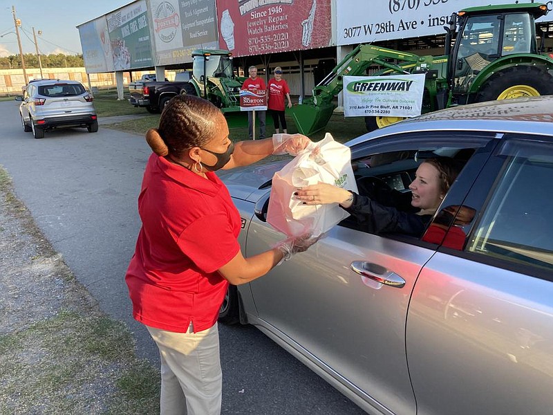 Tonya Shaw, a redcoat with the Pine Bluff Chamber of Commerce, hands a sack of fish and chicken dinners to a customer Thursday evening. This year’s fish fry was a drive-thru-only event because of concerns about the coronavirus. 
(Pine Bluff Commercial/Byron Tate)