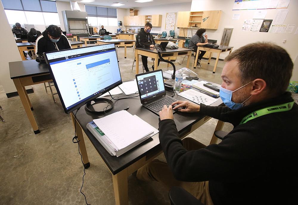 Mills High School chemistry teacher Dan Kahler talks with his virtual students via Zoom while his in-person students do their work Monday at the Little Rock school. Catering to the needs of in-person students while simultaneously instructing online students is like performing two jobs, some teachers say. (Arkansas Democrat-Gazette/Thomas Metthe)