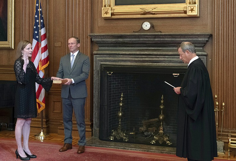 In this image provided by the Collection of the Supreme Court of the United States, Chief Justice John G. Roberts, Jr., right, administers the Judicial Oath to Judge Amy Coney Barrett in the East Conference Room of the Supreme Court Building, Tuesday, Oct. 27, 2020, in Washington as Judge Barrett's husband, Jesse M. Barrett, holds the Bible.