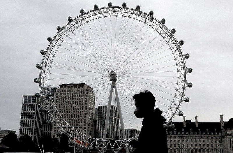 A man wears a face mask as he passes the London Eye in Britain on Thursday, Oct. 29, 2020.