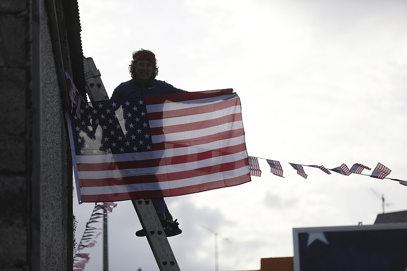 A man hangs a US flag up in the town of Ballina, North West of Ireland, Saturday, Nov. 7, 2020. Ballina is the ancestral home of US President elect Joe Biden. Biden was elected Saturday as the 46th president of the United States, defeating President Donald Trump in an election that played out against the backdrop of a pandemic, its economic fallout and a national reckoning on racism. (AP Photo/Peter Morrison)