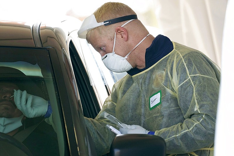 FILE - In this Oct. 28, 2020, file photo, a worker wearing gloves, a face shield, a mask, and other PPE administers a COVID-19 test at a King County coronavirus testing site in Auburn, Wash., south of Seattle. The latest surge in U.S. coronavirus cases appears to be larger and more widespread than the two previous ones, and it is all but certain to get worse. But experts say there are also reasons to think the nation is better able to deal with the virus than before, with the availability of better treatments, wider testing and perhaps greater political will. (AP Photo/Ted S. Warren, File)

