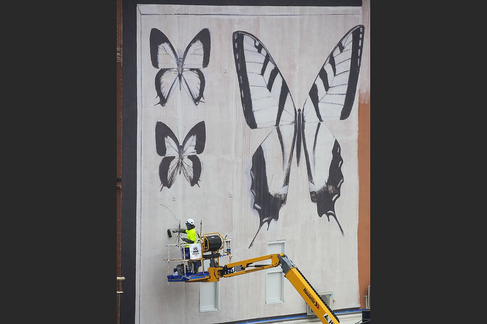French artist Youri Cansell starts his mural, depicting moths and butterflies, last month on the east wall of the River Market’s Ottenheimer Market Hall, 400 President Clinton Ave., Little Rock. The completed mural will be officially unveiled during Second Friday Art Night, 5-8 p.m. Friday. (Arkansas Democrat-Gazette/Staton Briedenthal)