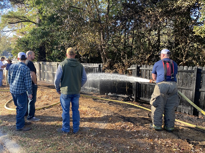 Emergency responders spray water after a fire destroyed a section of fenceline Monday on Columbia Street in Magnolia. No official statement on the cause of the blaze had been released at press time.
