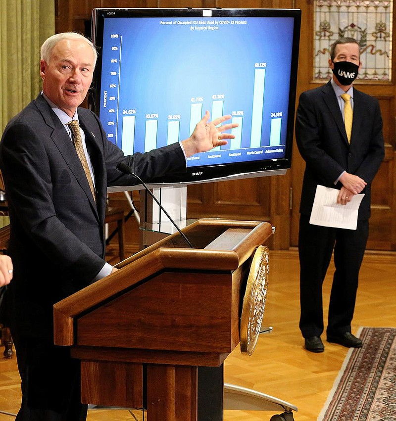 Gov. Asa Hutchinson discusses a chart showing the percentage of ICU beds being used by COVID-19 patients as Cam Patterson (right), chancellor of University of Arkansas for Medical Science, looks on during a press conference on Friday, Nov. 20, at the state Capitol in Little Rock. (Arkansas Democrat-Gazette/Thomas Metthe)