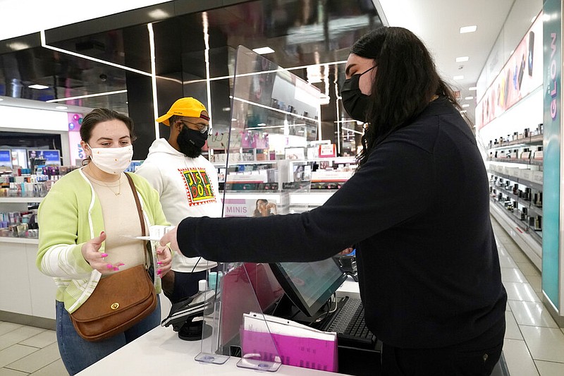 Cashier Druhan Parker, right, works behind a plexiglass shield Thursday, Nov. 19, 2020, as he checks out shoppers Cassie Howard, left, and Paris Black at an in Chicago.