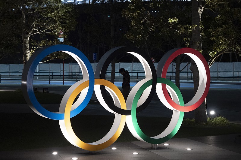 FILE - In this March 24, 2020, file photo, a man is seen through the Olympic rings in front of the New National Stadium in Tokyo. Tokyo Olympic organizers on Friday, Nov. 27, 2020 announced a series of 18 test events set to begin in March and run into May. 