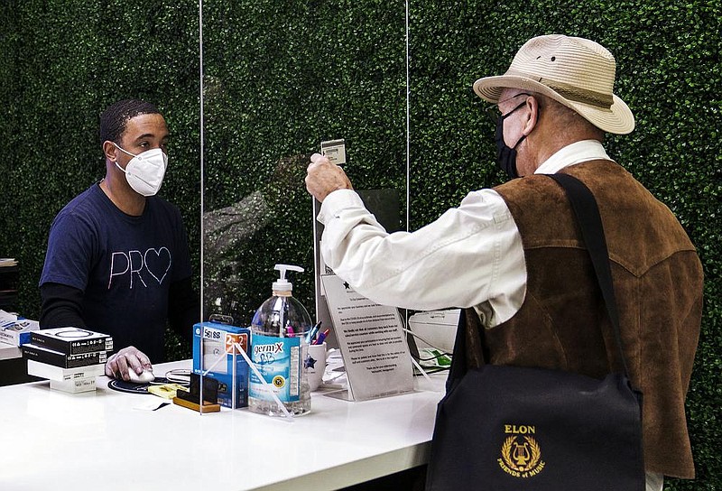 Melrose Mac Service coordinator Josh Smart (left) helps out Eric Hall make a contact-free purchase through a plastic-glass wall Friday at the store in Burbank, Calif. Los Angeles County, the nation’s most populous, has announced a new stay-home order taking effect Monday that advises residents to stay home “as much as possible” and to wear a face covering when they go out.
(AP/Damian Dovarganes)