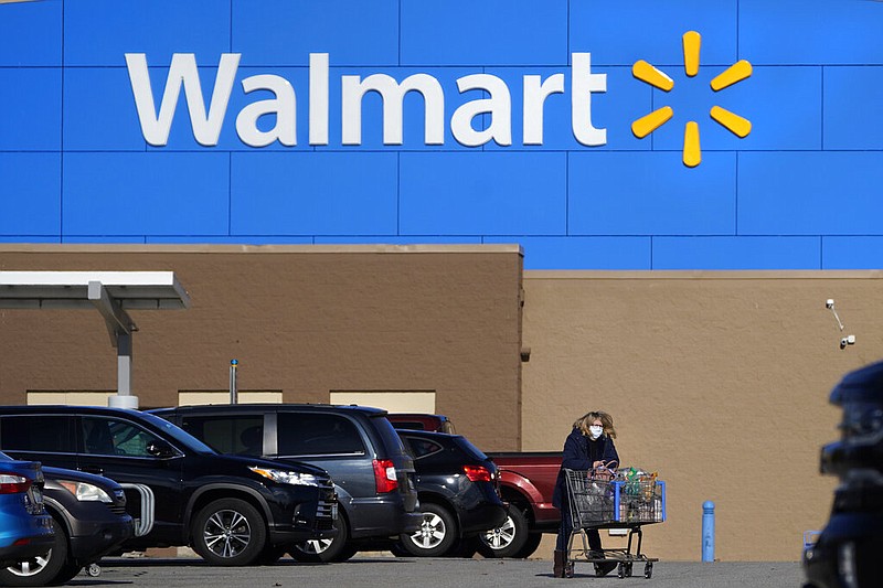 FILE - In this Nov. 18, 2020 file photo, a woman, wearing a protective face mask due to the covid-19 virus outbreak, wheels a cart with her purchases out of a Walmart store, in Derry, N.H.