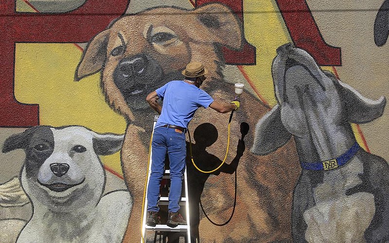 Artists Kevin Kresse works Thursday Dec. 10, 2020 in downtown North Little Rock putting a final coat of sealant on the new "Dogtown Proud" mural on a building at 4th and Main Streets. The mural is part of the downtown mural project for the Argenta Arts District. (Arkansas Democrat-Gazette/Staton Breidenthal)