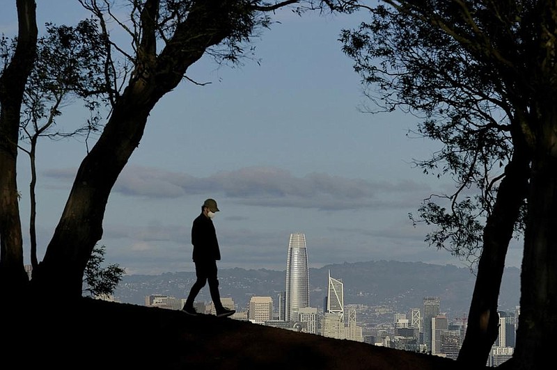 A man walks atop Tank Hill in front of the San Francisco skyline Thursday. California has been averaging 202 deaths a day recently, and the state has bought 5,000 extra body bags and set up 60 refrigerated storage units to help coroners, Gov. Gavin Newsom said Tuesday.
(AP/Jeff Chiu)