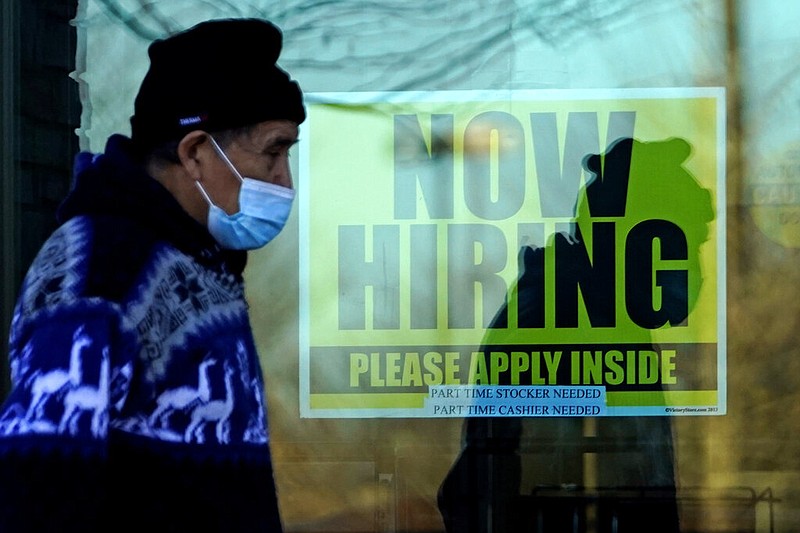 A shopper wearing a face mask walks past a store displaying a hiring sign in Wheeling, Ill., in this Nov. 28, 2020, file photo.