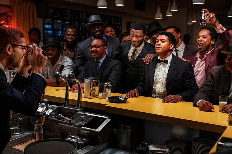 From behind the bar, Malcolm X (Kingsley Ben-Adir) photographs his friends football star Jim Brown (Aldis Hodge), tuxedo-clad boxer Cassius Clay (Eli Goree) and drink-raising singer Sam Cooke (Leslie Odom Jr.) in Regina King’s directorial debut “One Night in Miami.”