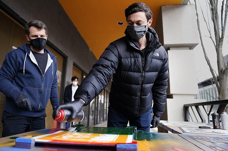 Jon Ossoff of Georgia, one of the two Democratic senators-elect criticized in an op-ed by South Dakota Gov. Kristi Noem, spray- paints a campaign poster Saturday with artist Brandon Litman in Atlanta. 
(AP/Brynn Anderson) 