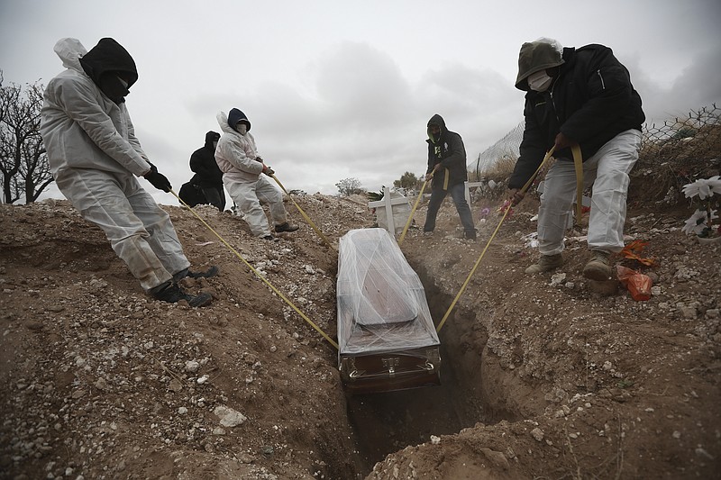 FILE - In this Oct. 27, 2020, file photo, workers wearing full protection gear amid the new coronavirus pandemic, lower a coffin into a grave in an area of the San Rafael municipal cemetery set apart for people who have died from COVID-19, in Ciudad Juarez, Mexico. The global death toll from COVID-19 has topped 2 million.