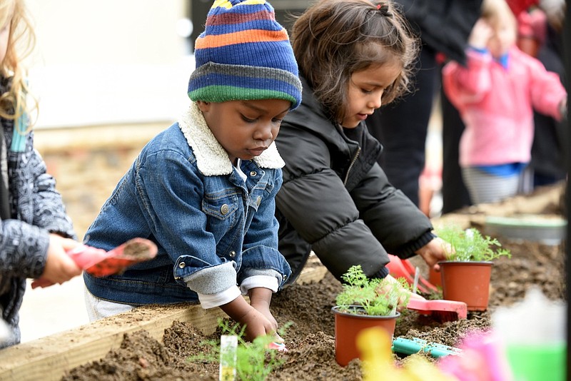 Arian Green (left), 2, and Victoria Arratia, 3, both students at The Goddard School Fayetteville, plant flowers Monday, March 25, 2019, with the guidance of volunteers from the Botanical Garden of the Ozarks at the school. The volunteers worked with two preschool classes and two prekindergarten classes and planted a flower bed and vegetable bed.