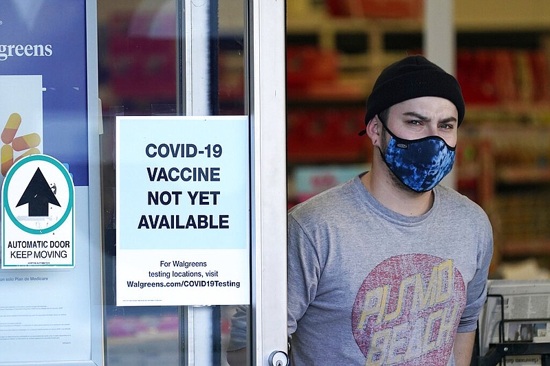 A customer wearing a mask walks out of a Walgreens pharmacy store in Seattle in this Dec. 2, 2020, file photo. At left, a sign advises that covid-19 vaccines were not yet available there.