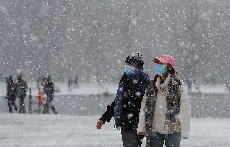 Pedestrians wearing face masks against the coronavirus pandemic walk in Kensington Gardens as snow falls in London, Sunday, Jan. 24, 2021. (AP Photo/Alastair Grant)