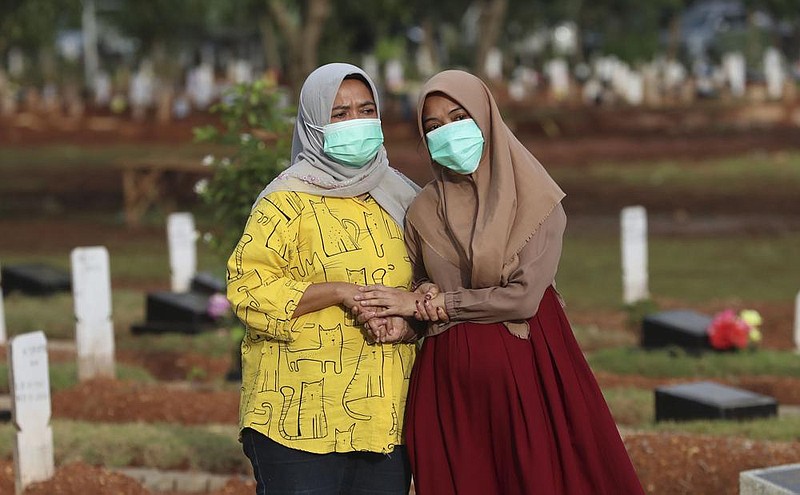 Women console each other Thursday in Bekasi, Indonesia, as a family member is buried in a section of the Padurenan cemetery designated to accommodate the surge in deaths during the coronavirus outbreak. More photos at arkansasonline.com/129covid19/.
(AP/Achmad Ibrahim)