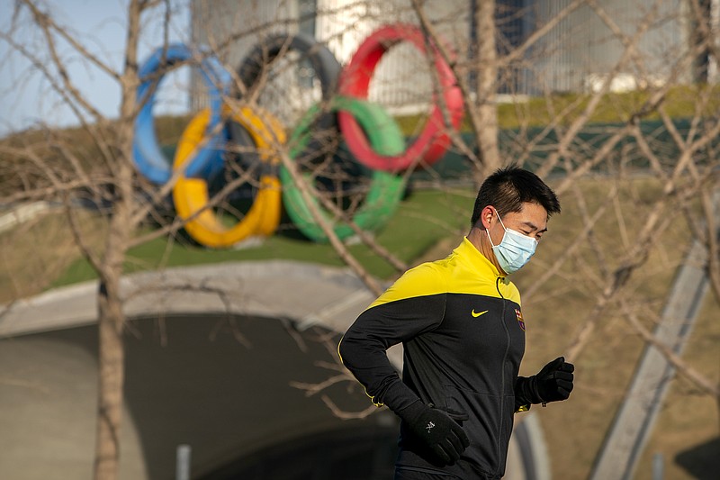 A man wearing a face mask to protect against the spread of the coronavirus jogs past Olympic rings displayed outside the Olympic Tower in Beijing, Tuesday, Feb. 2, 2021. The 2022 Beijing Winter Olympics will open a year from now. Most of the venues have been completed as the Chinese capital becomes the first city to hold both the Winter and Summer Olympics. Beijing held the 2008 Summer Olympics. But these Olympics are presenting some major problems. They are already scarred by accusations of rights abuses including "genocide"against more than 1 million Uighurs and other Muslim ethnic groups in western China. (AP Photo/Mark Schiefelbein) story.lead_photo.caption
