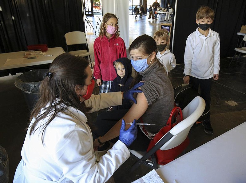Pharmacist Megan Smith, left,  gives Lauren Bolin her second covid-19 vaccine Friday Feb. 5, 2021 at the Pharmacy at Wellington in west Little Rock as her kids, background left to right, Sarah Elizabeth, 7, Thaddaeus, 2, Asa, 5, and Isaiah, 9, watch. (Arkansas Democrat-Gazette/Staton Breidenthal)