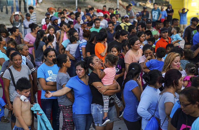 FILE - In this Aug. 30, 2019, file photo, migrants, many of whom were returned to Mexico under the Trump administration's "Remain in Mexico" policy, wait in line to get a meal in an encampment near the Gateway International Bridge in Matamoros, Mexico.