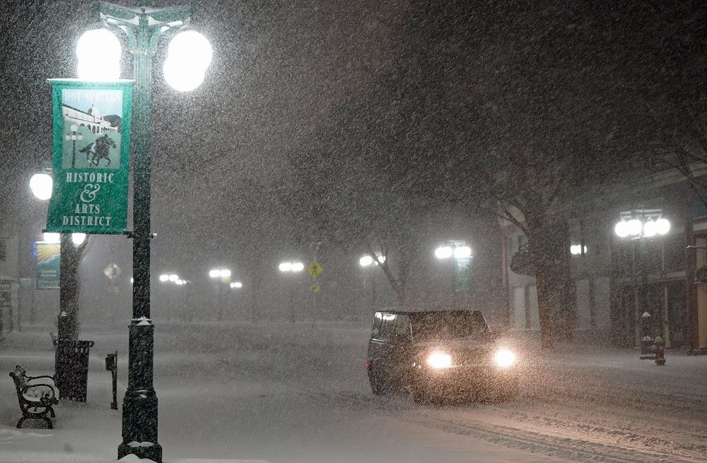 A lone car makes its way down Central Avenue in downtown Hot Springs Sunday night during a steady snowfall. - Photo by Cassidy Kendall of The Sentinel-Record