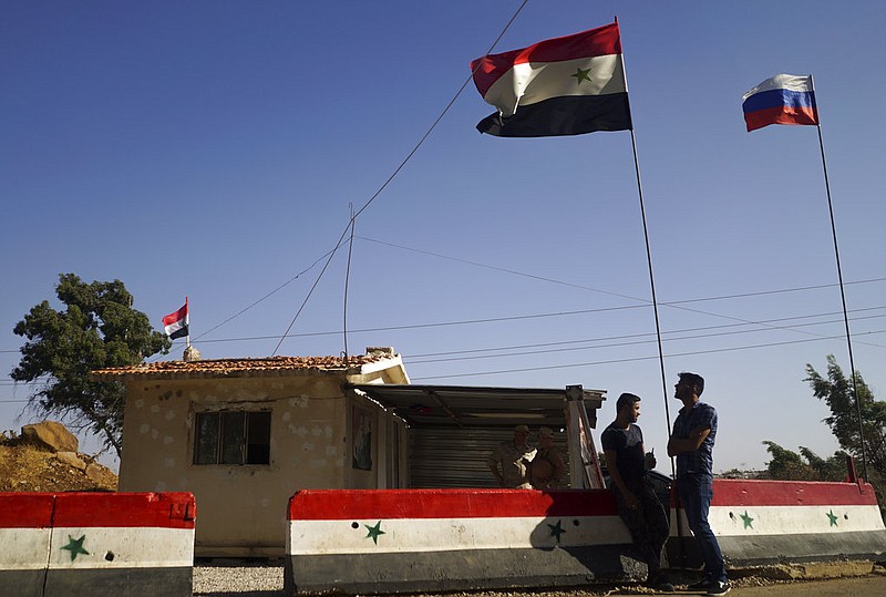 Syrians stand at a checkpoint in the de-escalation zone near Homs, Syria, as it flies both Syrian and Russian flags in this Sept. 13, 2017, file photo.