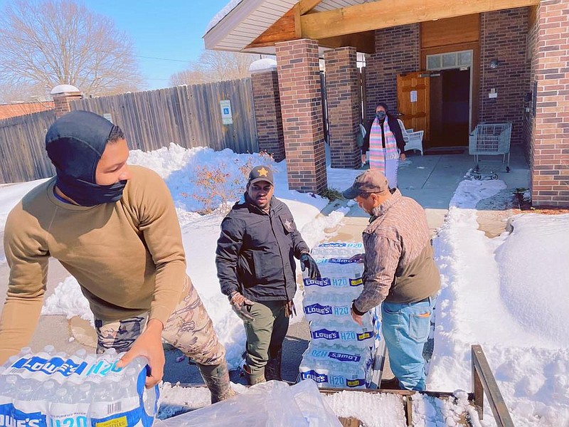 Jefferson County Deputy Cameron Johnson (from left), Sheriff Lafayette Woods and Sgt. Courtney Kelly unload 40 cases of water donated by Lowe’s on Friday to the CASA Women’s Shelter. Standing at the shelter door is agency board member Santrice Kearney. 
(Special to The Commercial)
