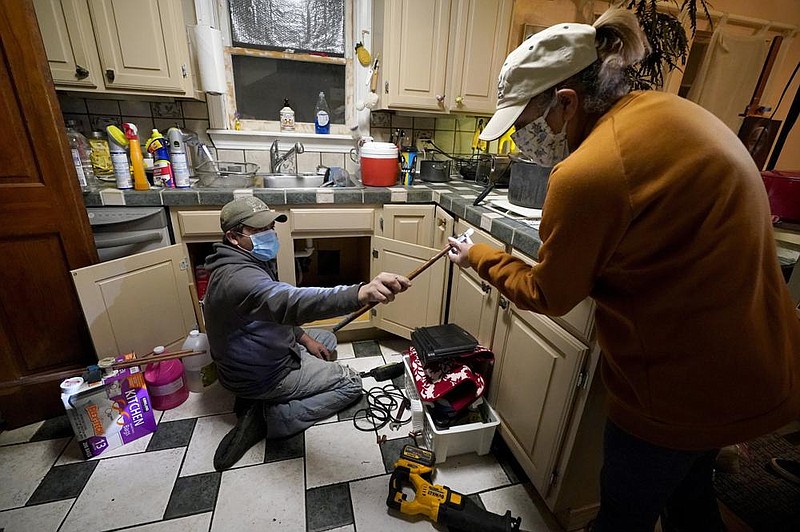 Handyman Roberto Valerio, left, hands homeowner Nora Espinoza the broken pipe after removing it from beneath her kitchen sink on Saturday, Feb. 20, 2021, in Dallas. The pipe broke during freezing temperatures brought by recent winter weather. (AP Photo/Tony Gutierrez)