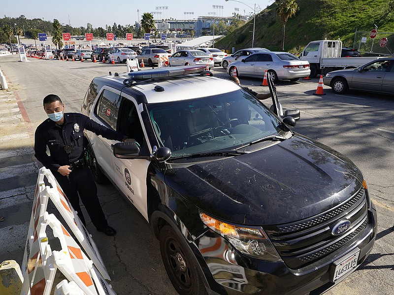 Los Angeles Police officers guard the main entrance to the vaccination center at Dodger Stadium as thousands of motorists wait in line for their vaccine without disruptions in Los Angeles Saturday, Feb. 27, 2021. A small group of anti-COVID-19 vaccine protestors demonstrated at a designated area in Elysian Park, outside the Dodger Stadium vaccination mass center. (AP Photo/Damian Dovarganes)