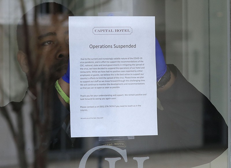 FILE — An employee puts a sign on the door in Little Rock at the Capital Hotel announcing that the hotel is suspending operations due to the corona virus in this Monday March 23, 2020 file phoot. (Arkansas Democrat-Gazette/Staton Breidenthal)