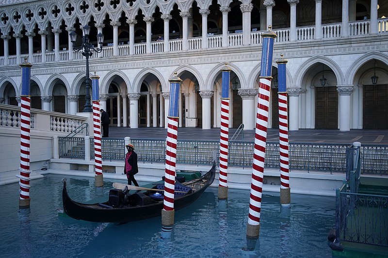 A gondolier stands by a boat near a quiet pedestrian walkway at the Venetian hotel and casino in Las Vegas, Feb. 4, 2021. The toll of the coronavirus is reshaping Las Vegas almost a year after the pandemic took hold. The tourist destination known for bright lights, big crowds, indulgent meals and headline shows is a much quieter place these days. (AP Photo/John Locher)