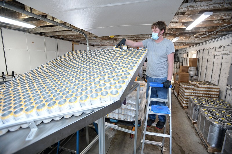 Jason Kramer, production executive at Black Apple, sends empty cans down a chute Tuesday, March 2, 2021, as he operates a canning machine at the facility located at 321 E. Emma Ave. in  Springdale. Black Apple is beginning to distribute its line of hard cider in Oklahoma. Visit nwaonline.com/210307Daily/ for today's photo gallery. .(NWA Democrat-Gazette/Andy Shupe)