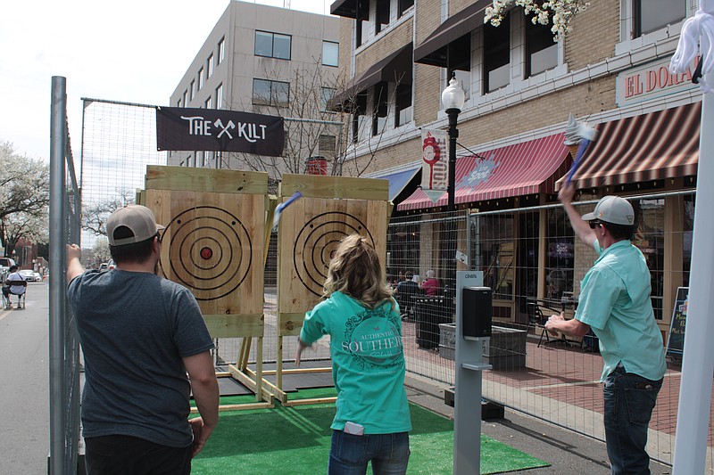 Ryan Thomas, owner of The Kilt - South Arkansas Axe Throwing, left, looks on as Autumn Kuntz, center, and Zachary Stanton try their hand at axe throwing during Shamrockin’ on the Square in downtown El Dorado Saturday. (Caitlan Butler/News-Times)