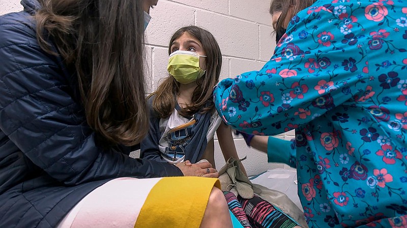 In this image from video provided by Duke Health, Alejandra Gerardo, 9, looks up to her mom, Dr. Susanna Naggie, as she gets the first of two Pfizer COVID-19 vaccinations during a clinical trial for children at Duke Health in Durham, N.C. In the U.S. and abroad, researchers are beginning to test younger and younger kids, to make sure the shots are safe and work for each age.