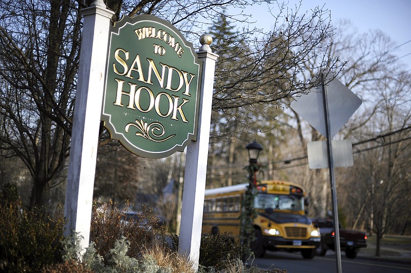 FILE - In this Dec. 4, 2013, file photo, a school bus drives past a sign reading Welcome to Sandy Hook, in Newtown, Conn., where 26 people were killed by a gunman inside Sandy Hook Elementary School. Students who were planning to attack schools showed the same types of troubled histories as those who carried them out - they were badly bullied, often suffered from depression with stress at home, and their behavior worried others, according to a U.S. Secret Service study released March 30, 2021.(AP Photo/Jessica Hill, File)