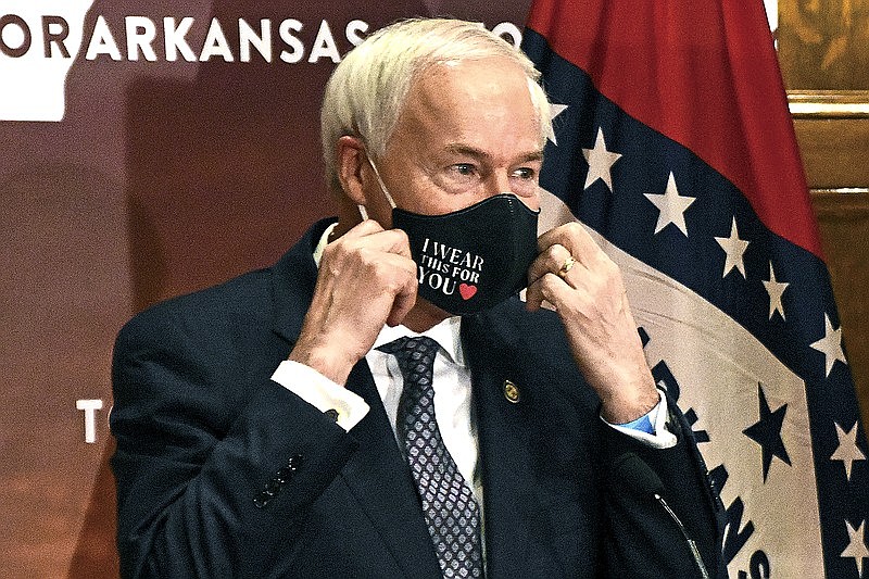 In this July 20 file photo, Gov. Asa Hutchinson removes his mask before a briefing at the state Capitol in Little Rock. (The Associated Press)