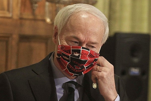 In this April 27, 2020 file photo, Gov. Asa Hutchinson takes off his Arkansas Razorbacks facemask as he arrives for the daily coronavirus briefing at the state Capitol in Little Rock.