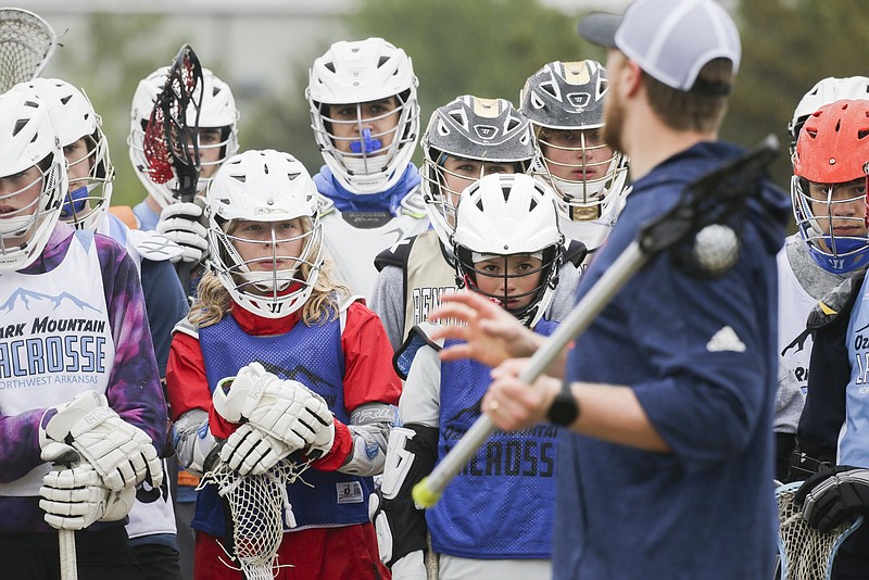 Students listen as professional lacrosse player, Tom Schreiber, gives instructions on technique, Friday, April 16, 2021 during a lacrosse clinic at Phillip's Park in Bentonville. Lacrosse is a rapidly growing sport in Northwest Arkansas. The Ozark Mountain Lacrosse program held a clinic for players in grades 7-12. Check out nwaonline.com/210417Daily/ for today's photo gallery. .(NWA Democrat-Gazette/Charlie Kaijo)