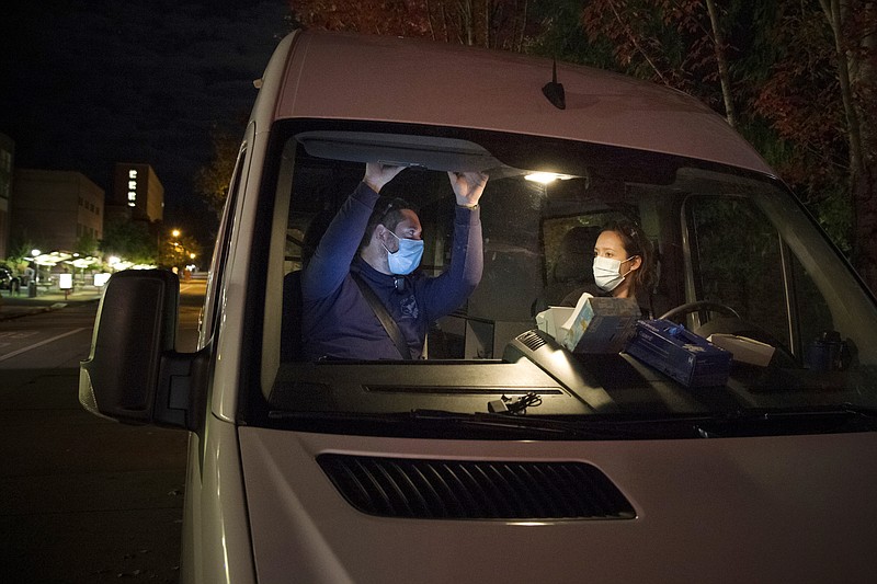 In this Oct. 2020 photo, Crisis Workers, Emergency Medical Technicians (EMTs), Henry Cakebread and Ashley Barnhill-Hubbard with CAHOOTS, a mental health crisis intervention program, discuss their last encounter during their night shift in Eugene, Ore. When police respond to a person gripped by a mental health or drug crisis, the encounter can have tragic results. Now a government health program will help communities set up an alternative: mobile teams of practitioners trained in de-escalating such potentially volatile situations. (William Holderfield via AP)